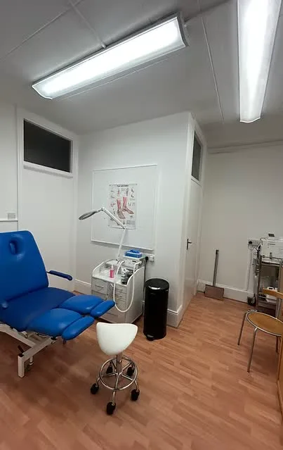 The treatment room: a blue podiatry chair, an examination lamp, an instrument trolley and a foot anatomy poster.