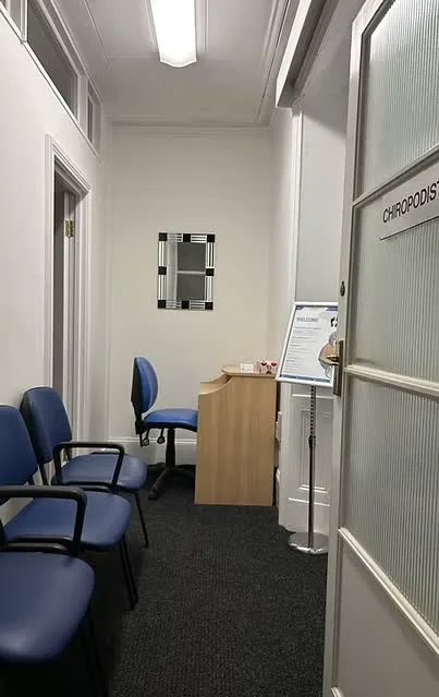 The waiting area with blue chairs, a reception desk and a frosted glass door marked chiropodist.